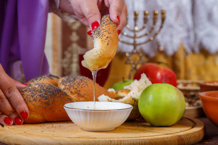 A woman's hand dips a piece of challah in honey at a set table on the Jewish holiday of Rosh Hashanah after prayer. Horizontal photo.の写真素材