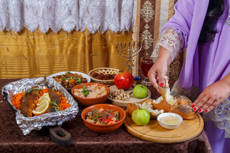 A woman's hand dips a piece of challah in honey at a set table on the Jewish holiday of Rosh Hashanah after prayer. horizontal photoの写真素材