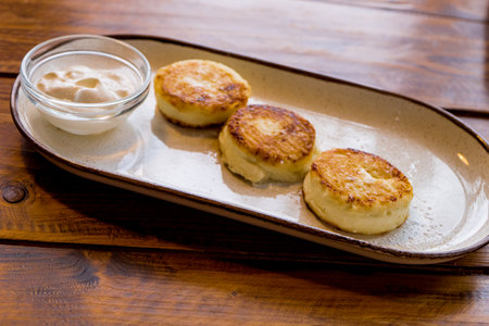 Hot cheesecakes with sour cream sprinkled with sugar on a plate on a wooden table. horizontal photoの写真素材
