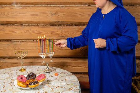 A Jewish woman lights Hanukkah candles at a table with donuts. horizontal photoの写真素材