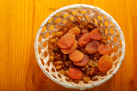 Dried apricots and raisins in a wicker plate on a wooden table. Horizontal photo.の写真素材