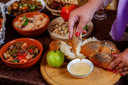 A woman's hand dips a piece of challah in honey at a set table on the Jewish holiday of Rosh Hashanah after prayer. horizontal photoの写真素材