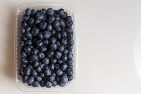 Fresh juicy blueberries in a transparent plastic container with a slide on a white table. horizontal photoの写真素材