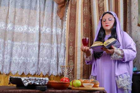 A Jewish woman in a wig and a veil falling from her hair makes kiddush for wine on Rosh Hashanah, Shabbat at the set table Horizontal photoの写真素材