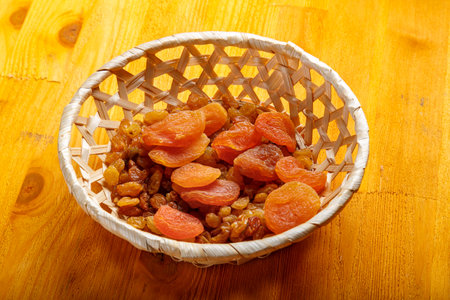 Dried apricots and raisins in a wicker plate on a wooden table. Horizontal photo.の写真素材