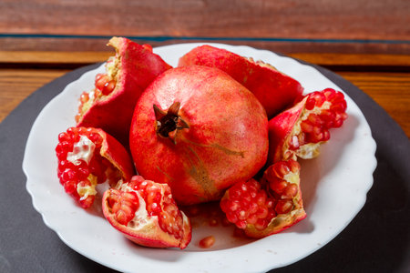 Fresh juicy pomegranate broken with grains and a whole fruit on a white plate. Close-up Horizontal photoの写真素材