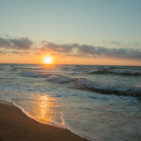 Sunrise from behind the horizon over the seas golden water and sandy shore. Square frameの写真素材