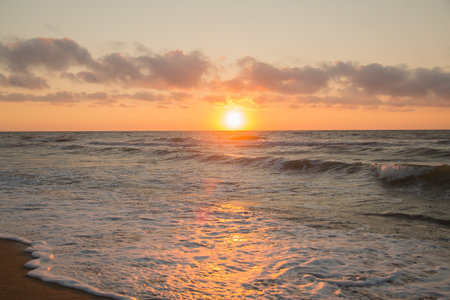 Sunrise from behind the sea, golden water and the edge of the coast in white waves. horizontal photoの写真素材