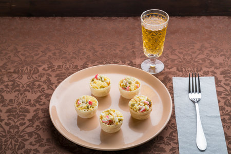 Champagne sparkling in a glass next to a plate with salad in tartlets on a brown tablecloth. Horizontal photo.の写真素材