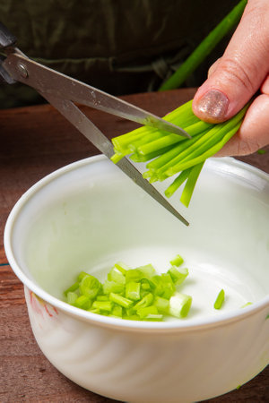 Green onions and feathers are cut with scissors by a woman's hand into a white salad bowl. Vertical photo.の写真素材