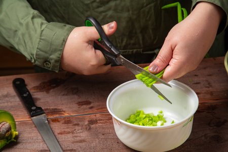Green onions and feathers are cut with scissors by a woman's hand into a white salad bowl. Horizontal photo.の写真素材