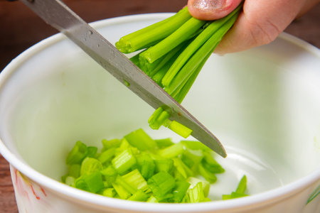 Green onions are cut with scissors into a white salad bowl. Horizontal photo.の写真素材
