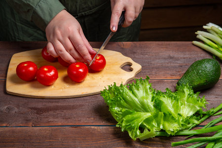 A cherry tomato is cut in half with a knife on a wooden board on the table. horizontal photoの写真素材