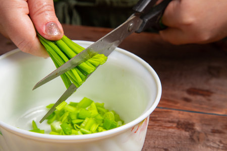 Green onions are cut with scissors into a white salad bowl. Horizontal photo.の写真素材