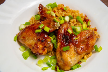 Chicken wings baked with bulgur, colored with green onions on a white plate, close-up. horizontal photoの写真素材