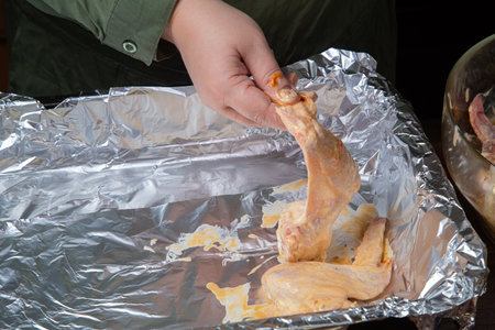 a woman's hand places chicken wings in soy sauce and garlic marinade on foil for baking. Horizontal photo.の写真素材