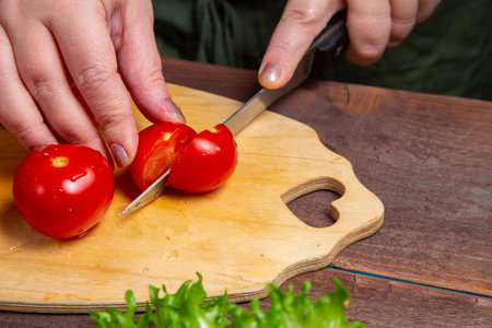 Cherry tomato is cut with a knife on a wooden board on a plank table. Horizontal photo.の写真素材