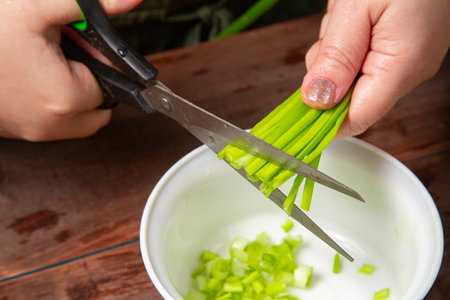 Green onions are cut with scissors into a white salad bowl. Horizontal photo.の写真素材