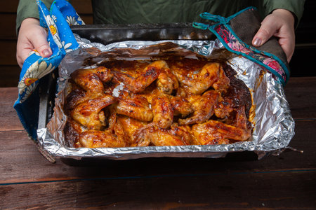 woman's hands hold a baking sheet with chicken wings baked on foil. Horizontal photo.の写真素材