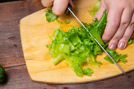 A woman's hand cuts greens with a knife on a board on a table with vegetables. Horizontal photo.の写真素材