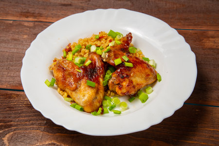 Chicken wings baked with bulgur, topped with green onions, garnished with cherry tomatoes on a white plate. Horizontal photo.の写真素材