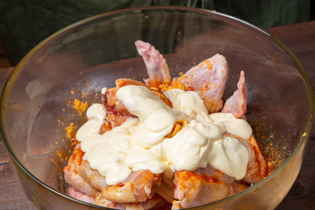 A thick, creamy sauce is poured into a glass plate filled with golden-spiced chicken wings. horizontal photoの写真素材
