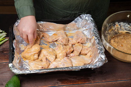 A woman s hand places Chicken wings in soy sauce and garlic marinade on foil. horizontal photoの写真素材