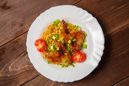 Chicken wings baked with bulgur, topped with green onions and garnished with cherry tomatoes. Horizontal photo.の写真素材
