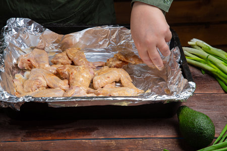 A woman s hand places Chicken wings in soy sauce and garlic marinade on foil. horizontal photoの写真素材