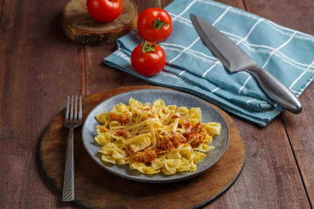 Bolognese pasta on a wooden round stand next to a knife and tomatoes on a napkin. Horizontal photo.の写真素材