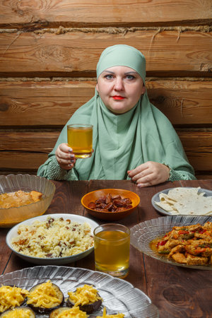 A young Muslim woman in a light khimar drinks uzwar at the table during Iftar Ramadan. Vertical photoの写真素材
