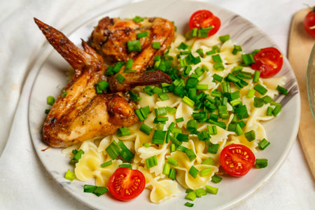 Farfalle pasta with grilled chicken wings on a white plate garnished with cherry tomatoes and green onions. Medium plan.の写真素材