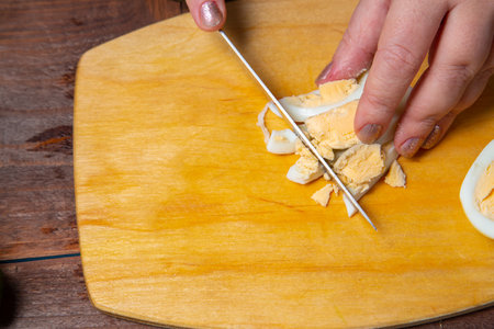 A chicken egg is cut finely with a knife on a wooden board. horizontal photoの写真素材