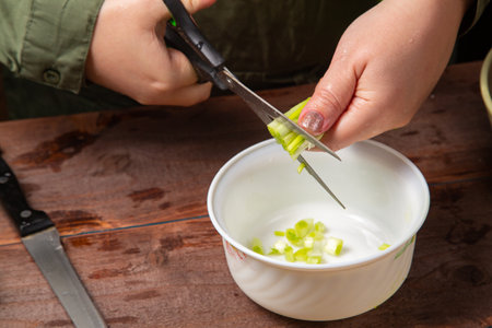 Green onions and feathers are cut with scissors by a woman's hand into a white salad bowl. Horizontal photo.の写真素材