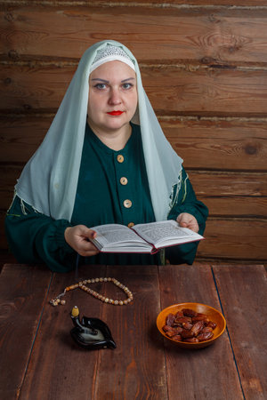 A Muslim woman reads the Koran at the table at night before the end of the Ramadan fast on the table with dates and incense. Vertical photoの写真素材