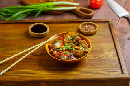 Thai chicken with rice and vegetables in a wooden plate on a wooden table next to soy sauce sticks...