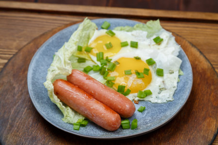 Scrambled two eggs with sausages sprinkled with green onions on a gray plate. Horizontal photo.の写真素材
