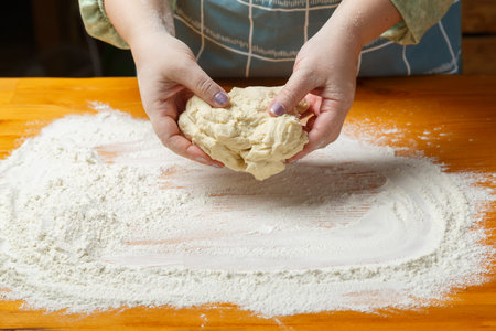 Women's hands knead the dough on a table sprinkled with flour. horizontal photo