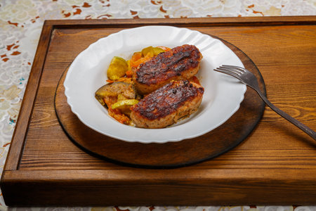 Beef cutlet with fried vegetables on a white plate on a hearth table next to a fork. Horizontal...