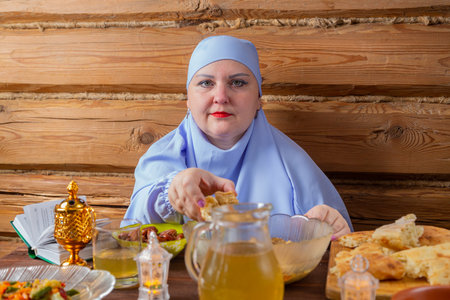 A Muslim woman in a blue hijab at the Eid al Fitr table takes a flatbread. horizontal photoの写真素材