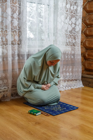 A Muslim woman in a light prayer dress kneeling on a mat makes a bow. Vertical photo.の写真素材