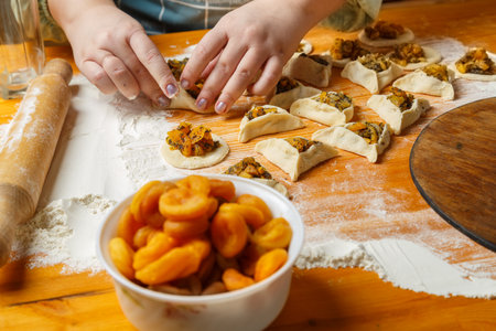 Women's hands mold triangle gomentashi cookies, a treat for the holiday of Purim, next to flour, a...