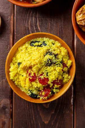 couscous with dried fruits in a wooden bowl next to the dogwood on the table. Vertical photo.の写真素材