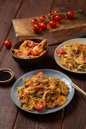 Rice with shrimp and udon noodles in yaki soba sauce on a wooden table next to cherry tomatoes, soy sauce and chopsticks. Vetical photoの写真素材