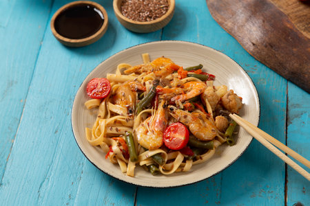 shrimp and udon vegetables pad thai sauce and chopsticks and soy sauce on a blue table. copy space. horizontal photoの写真素材