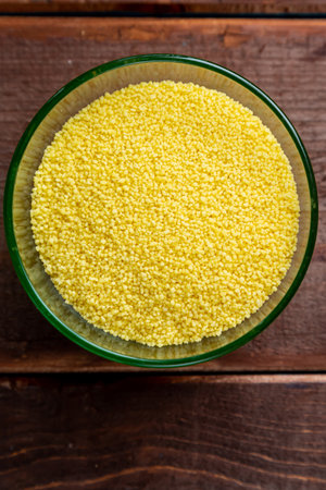 Crumbled couscous cereal in a glass bowl on a wooden table. Vertical photo