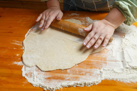 A woman's hand rolls out dough with a rolling pin on a table sprinkled with flour. horizontal photo
