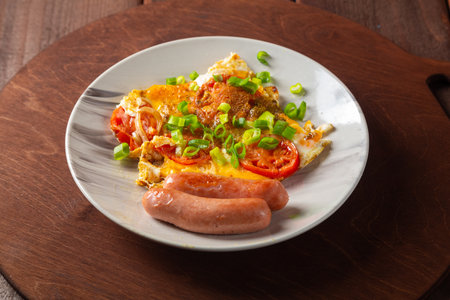 Eggs with tomatoes and fried sausage in a plate on a round wooden stand. horizontal photoの写真素材