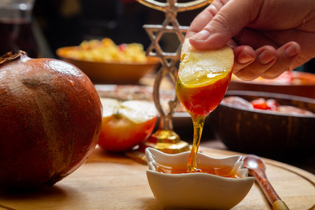 A woman's hand at the table during the Rosh Hashanah holiday dips an apple in honey. Horizontal photo.の写真素材