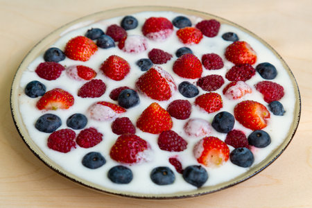 In a plate with whipped cream, strawberries, raspberries and blueberries on the table. Horizontal photo.の写真素材